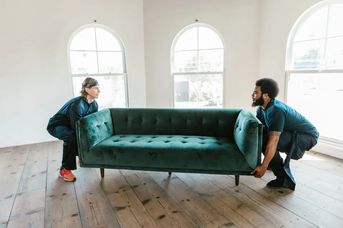 Two workers carrying a green sofa across a room