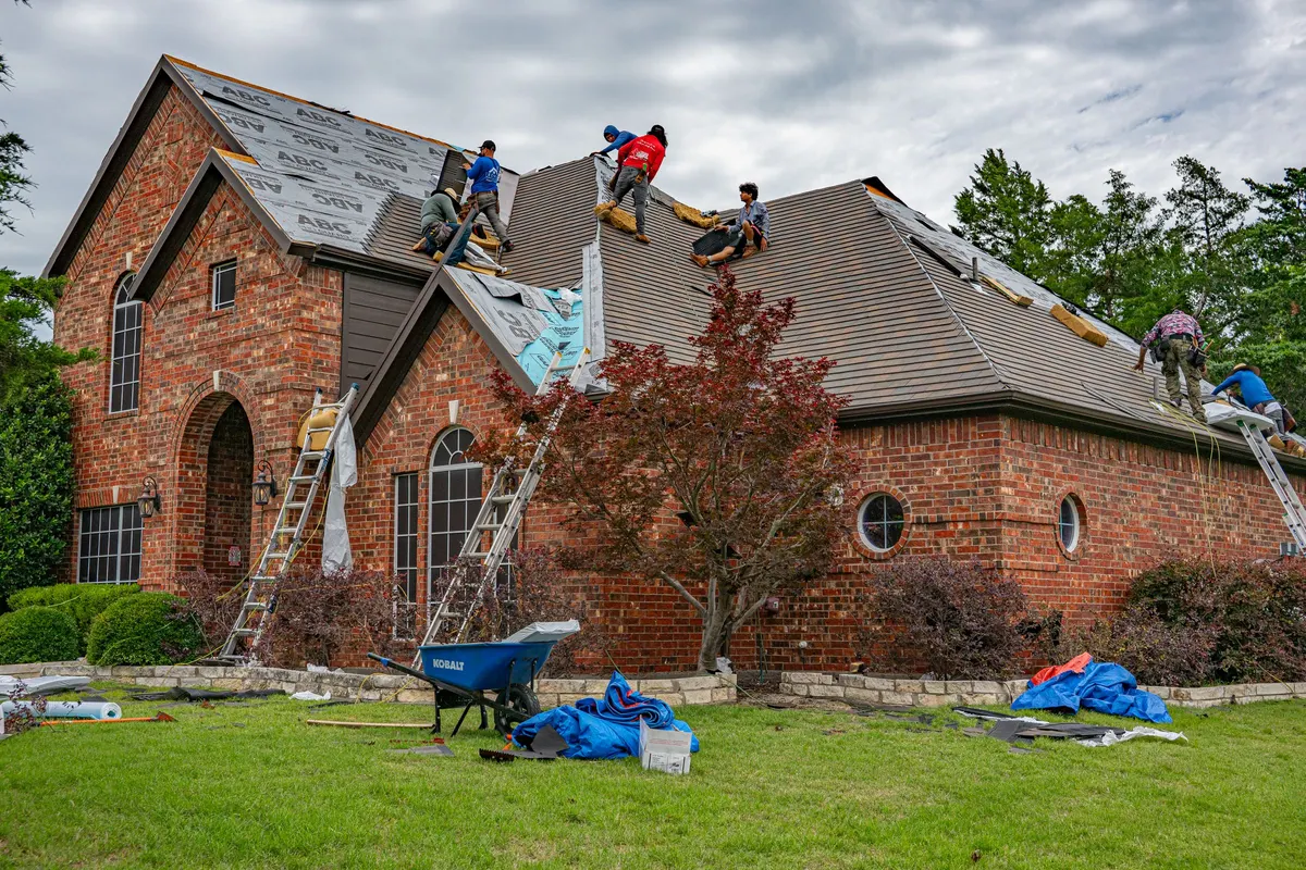 Workers on the roof of a brick house during a roof tear-off